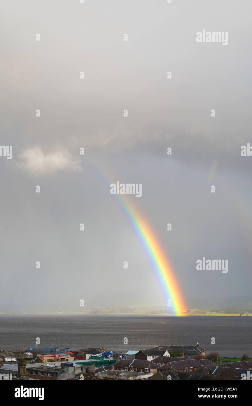 Bright rainbow high in sky over the sea during dark storm Stock Photo