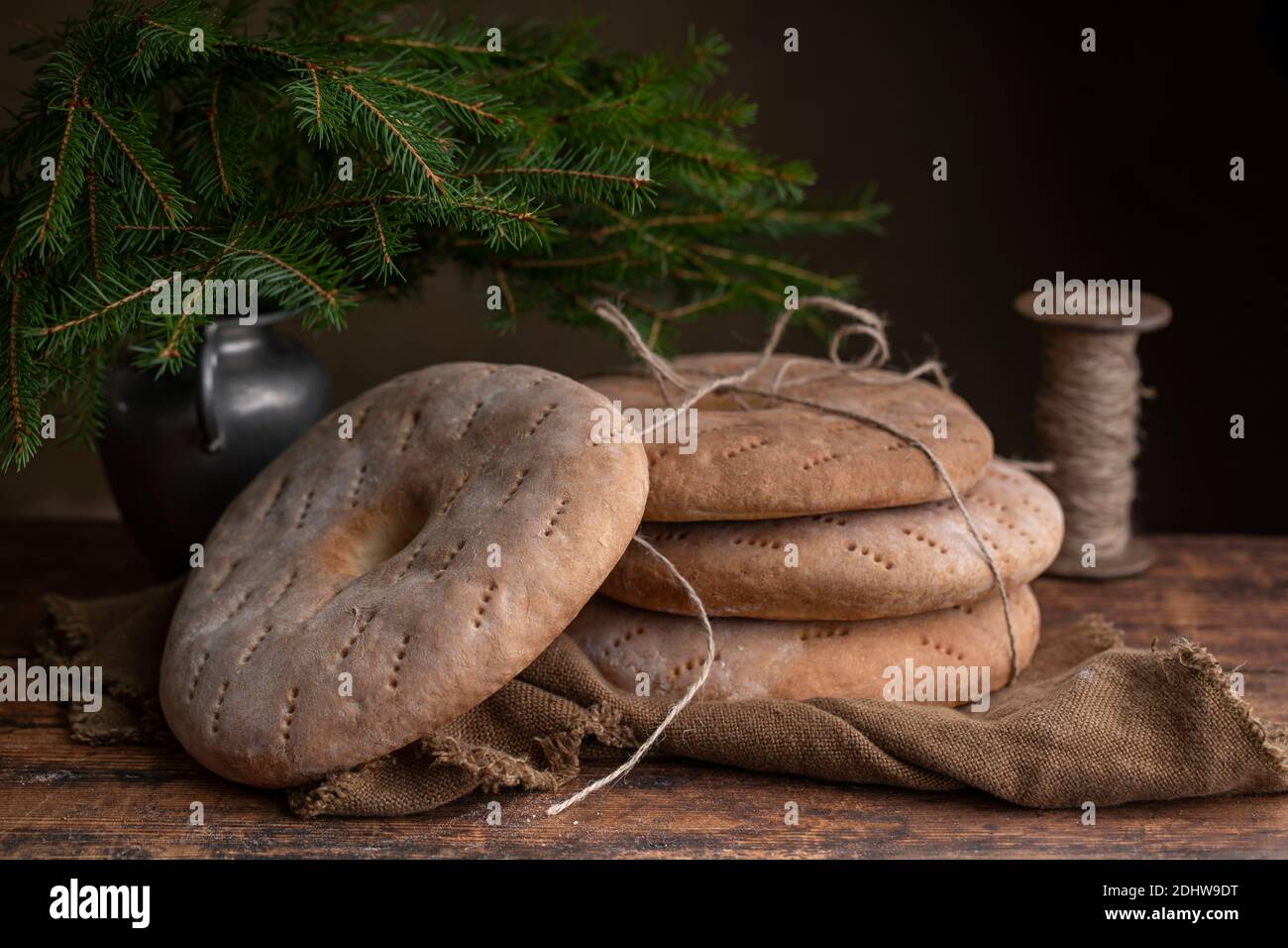Four round breads with hole in the middle, some of them are tied by a jute cord. Old fashioned rye sieve breads. On a retro brown table, with a vase w Stock Photo
