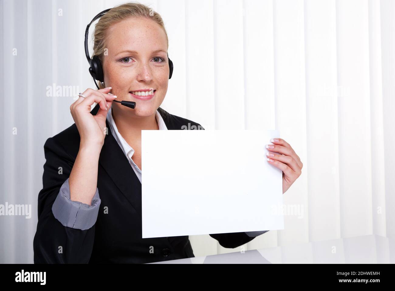 Eine freundliche junge Frau mit Headset im Kundendienst telefoniert mit einem Kunden. Freundliche Hotline Mitarbeiterin. Stock Photo