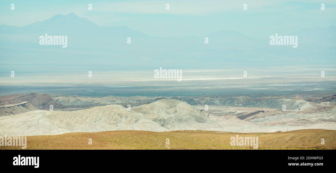 Salt pans and volcanoes in the distance with the rocky desert hills of the Atacama Desert in the foreground Stock Photo