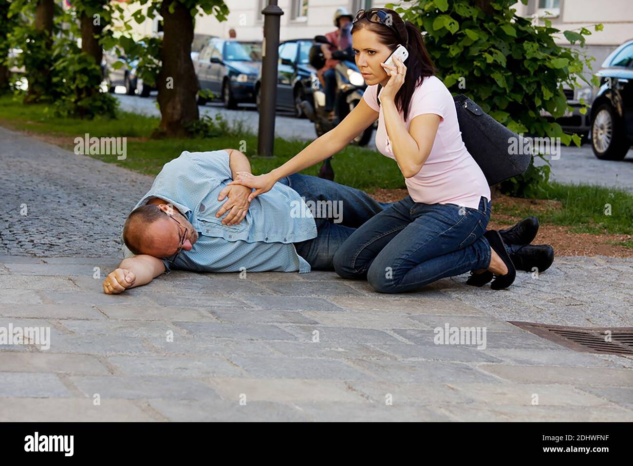 Ein Mann hat einen Schwindelanfall oder einen Herzanfall. Eine Frau kommt zu Hilfe. Stock Photo