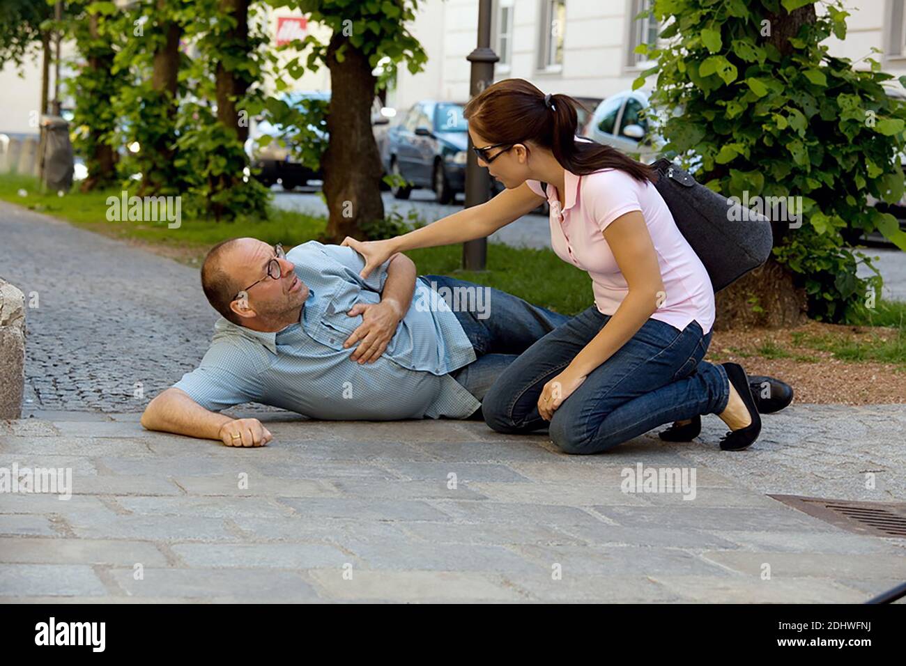 Ein Mann hat einen Schwindelanfall oder einen Herzanfall. Eine Frau kommt zu Hilfe. Stock Photo
