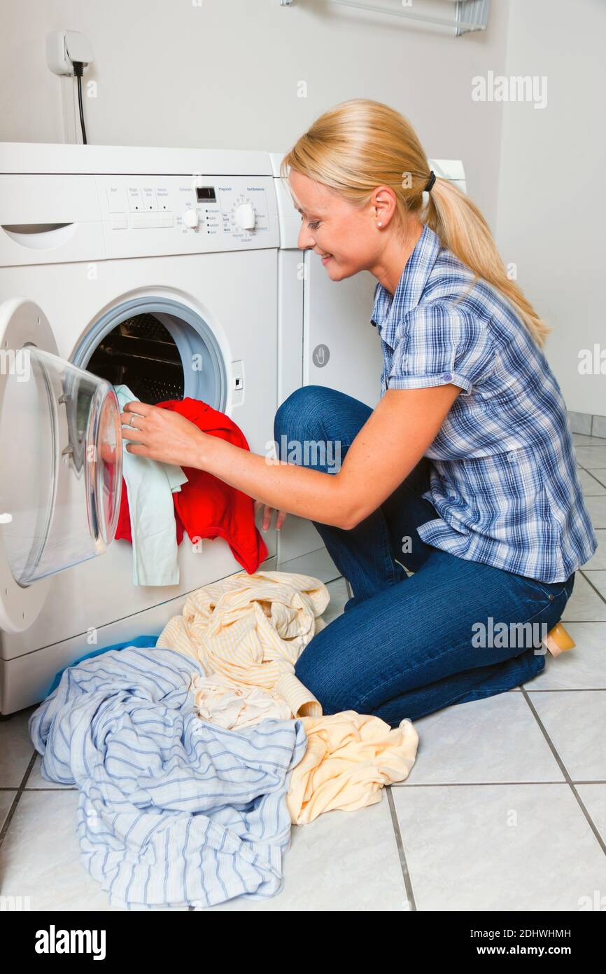 Eine junge Hausfrau mit Waschmaschine und Wäsche hat einen Waschtag. Stock Photo