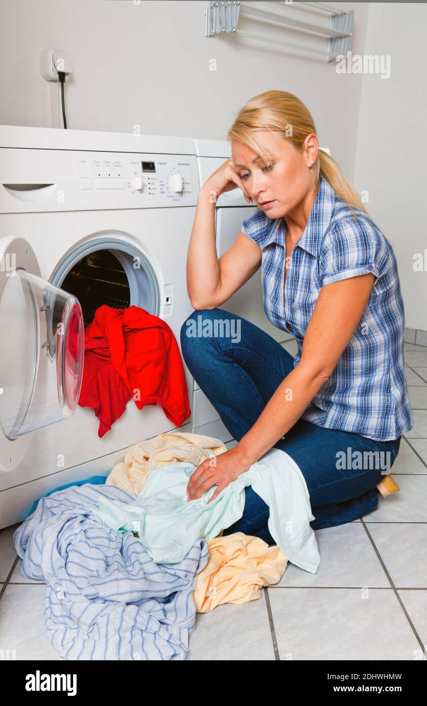 Eine junge Hausfrau mit Waschmaschine und Wäsche hat einen Waschtag. Stock Photo