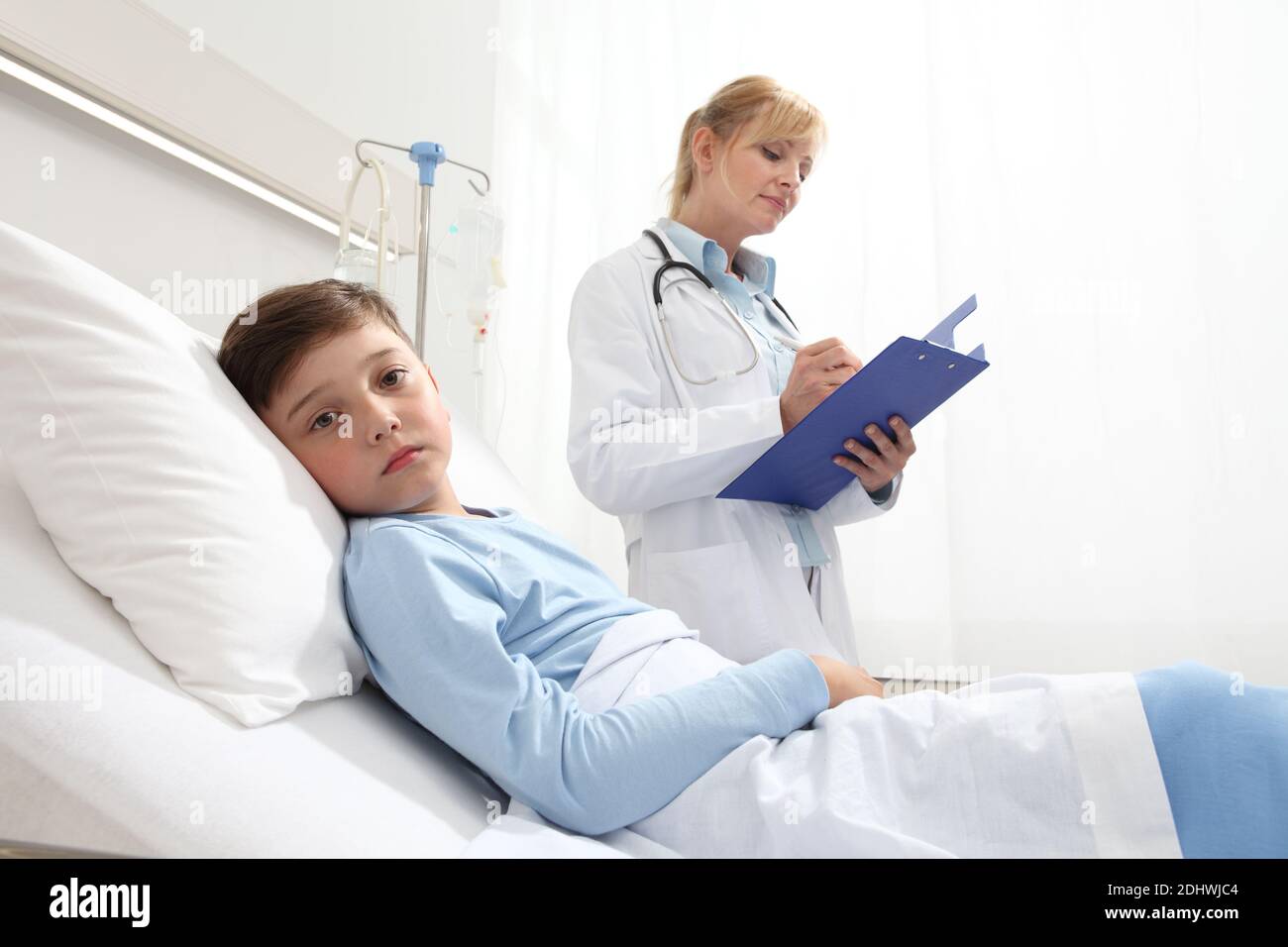 Sick child lying in bed in hospital room looking at camera with doctor