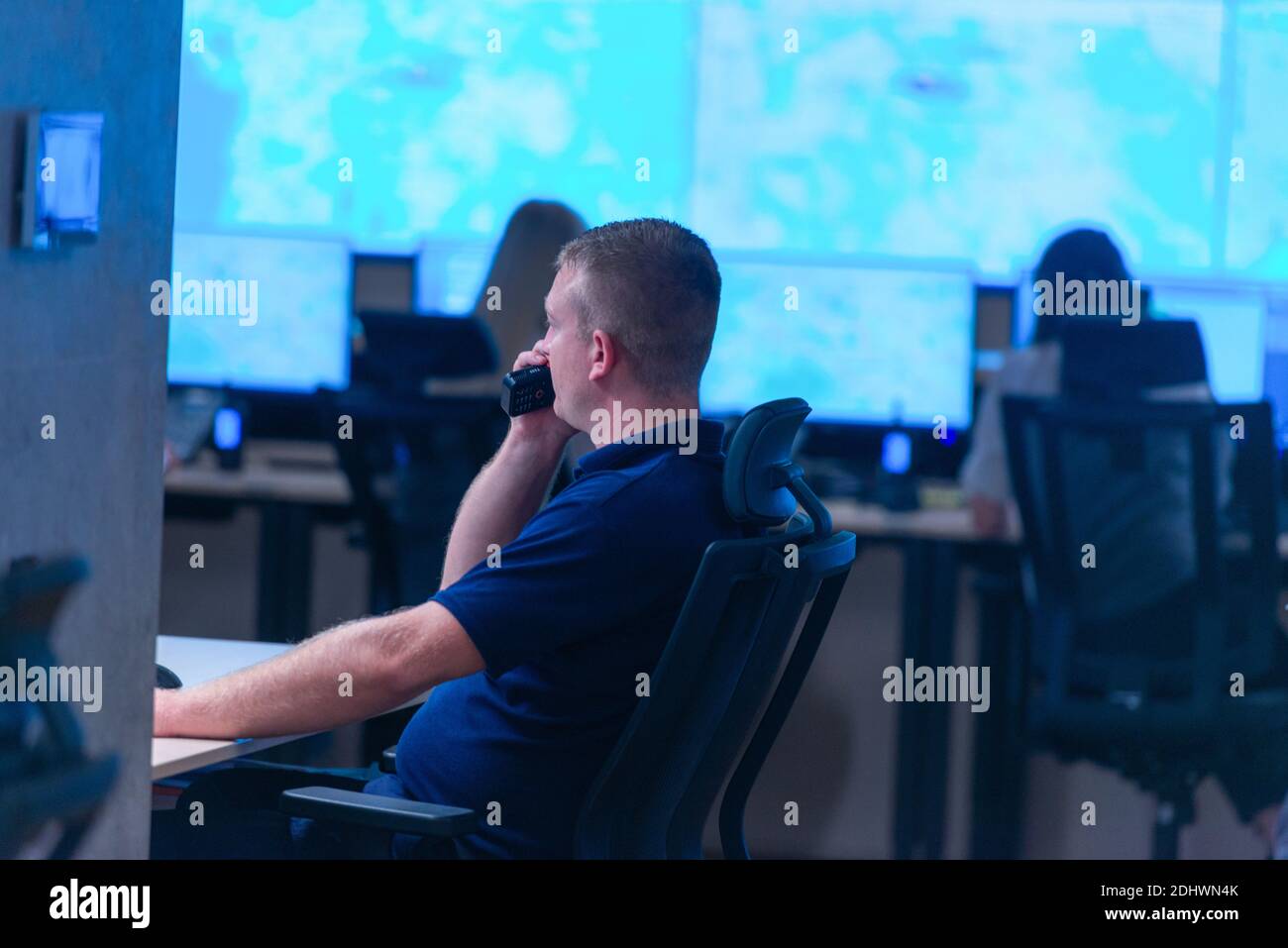Side view of security system operator using walkie-talkie while looking at CCTV footage Stock Photo