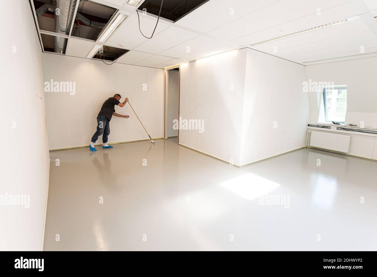 LAREN, THE NETHERLANDS - MAY 16, 2012: Construction workers applying a new layer of an indoor synthetic cast coating floor with a large roller Stock Photo