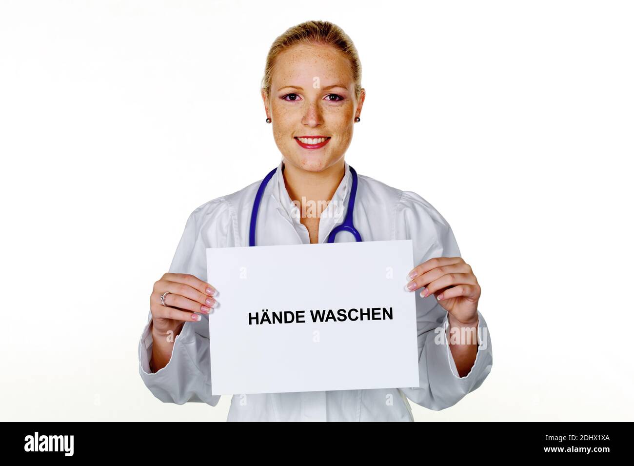 Eine junge Aerztin mit Stethoskop in ihrer Arztpraxis. Haelt ein leeres Schild mit der Aufschrift: Haende waschen Stock Photo