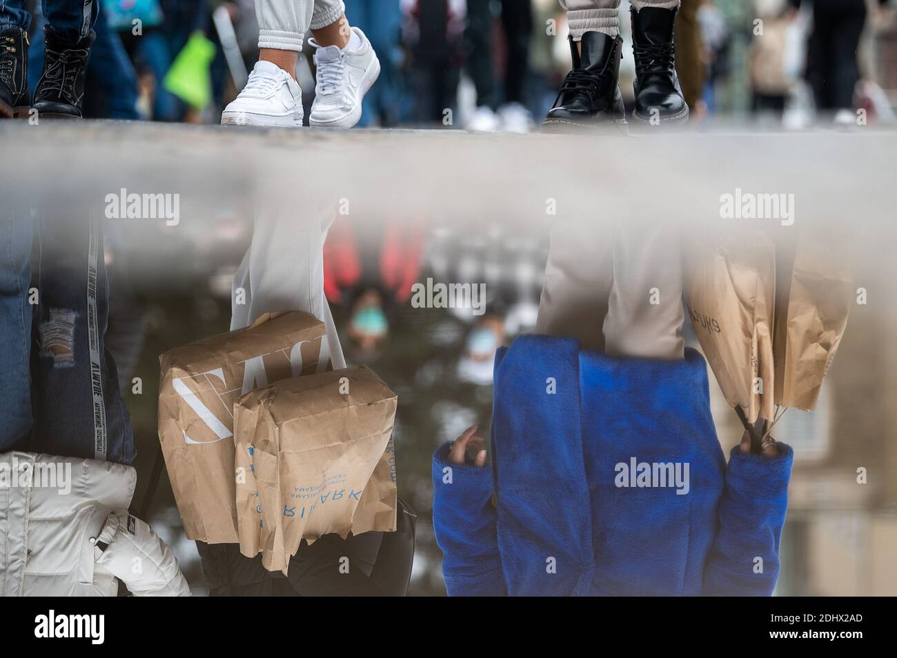 Stuttgart, Germany. 12th Dec, 2020. Passers-by shopping in the city centre are reflected in a puddle. Since 12 December 2020, exit restrictions have been in force in Baden-Württemberg. In the pre-Christmas period, the retail trade is still allowed to open during the day despite the corona-related exit restrictions. Credit: Sebastian Gollnow/dpa/Alamy Live News Stock Photo