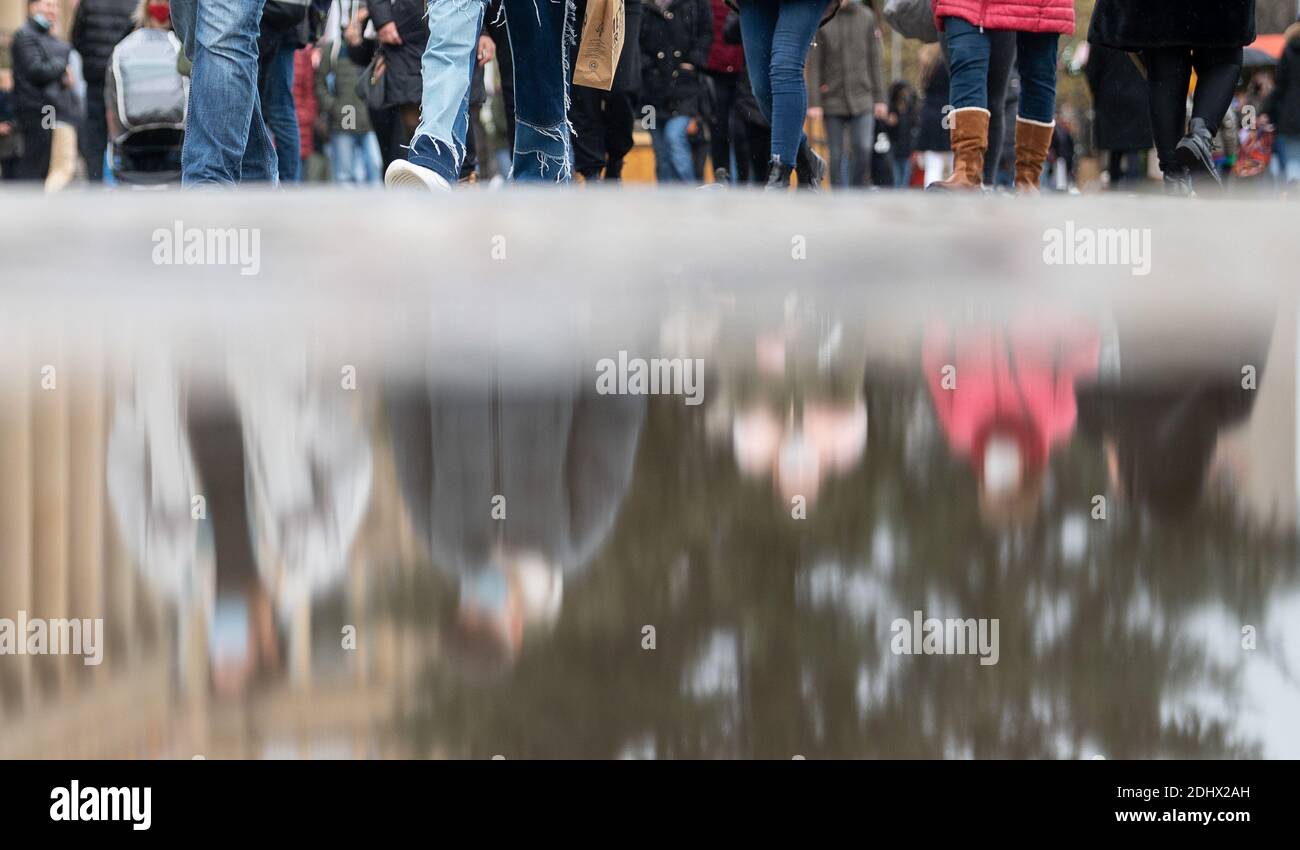 Stuttgart, Germany. 12th Dec, 2020. Passers-by shopping in the city centre are reflected in a puddle. Since 12 December 2020, exit restrictions have been in force in Baden-Württemberg. In the pre-Christmas period, the retail trade is still allowed to open during the day despite the corona-related exit restrictions. Credit: Sebastian Gollnow/dpa/Alamy Live News Stock Photo