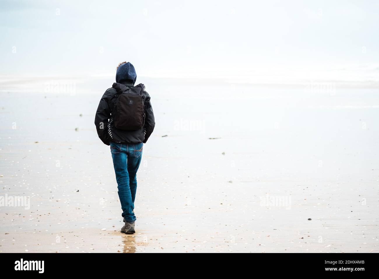 A young man with a backpack wearing a hoodie walks on the beach Stock ...