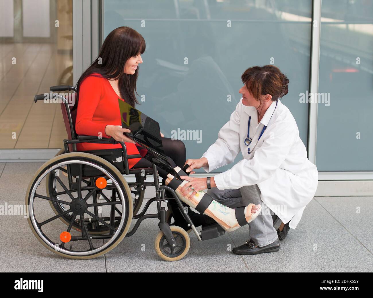 Junge Frau mit Gipsbein sitzt im Rollstuhl, MR: Yes, Aerztin versorgt. sie, Stock Photo