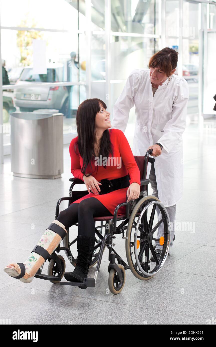 Junge Frau mit Gipsbein sitzt im Rollstuhl, MR: Yes, Aerztin versorgt. sie, Stock Photo