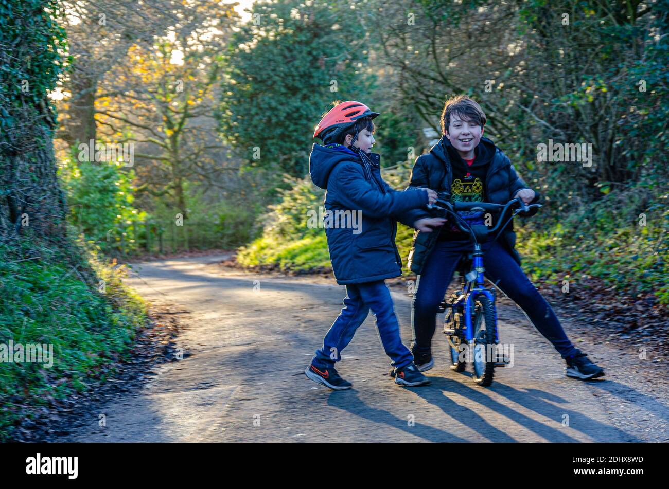 An older brother sits on his younger brothers bicycle down a country lane. Stock Photo