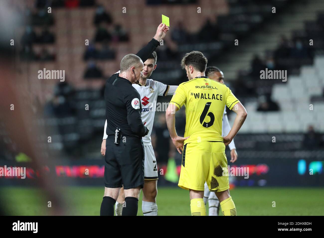 MILTON KEYNES, ENGLAND. DECEMBER 12TH. Graham Salisbury shows a yellow card  to Burton Albion's Kieran Wallace during the second half of the Sky Bet  League One match between MK Dons and Burton
