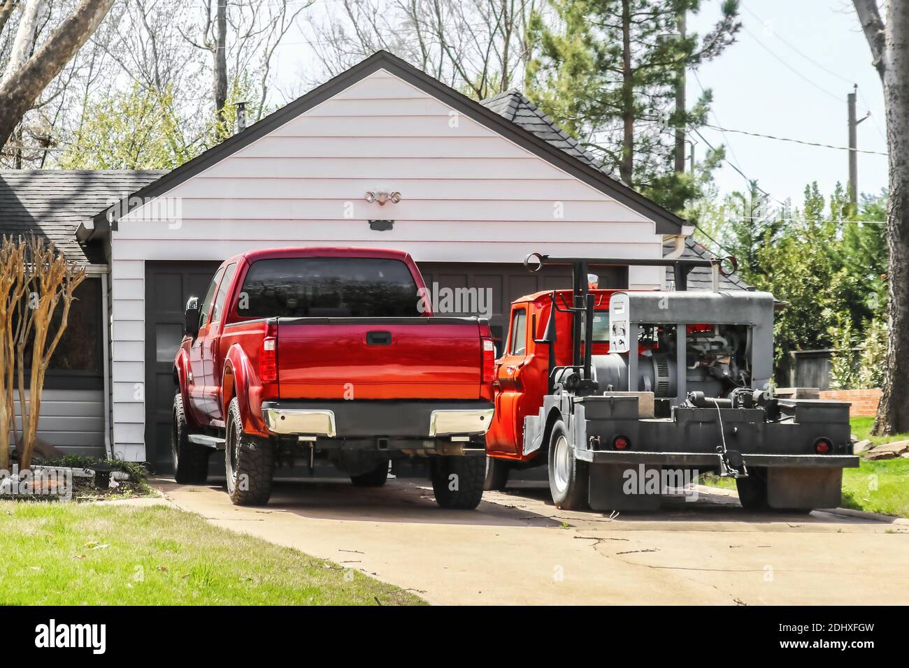 Red pickup truck and older red truck with welder on the back parked in the driveway in front of a residential garage and house Stock Photo