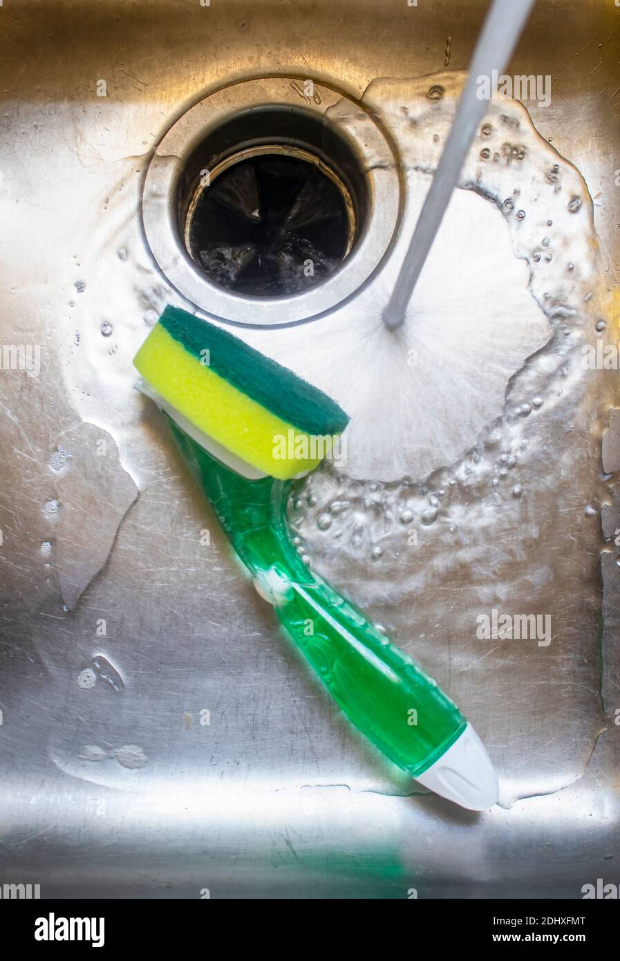 Water from tap running into stainless steel sink with pot scrubber lying in it. Stock Photo