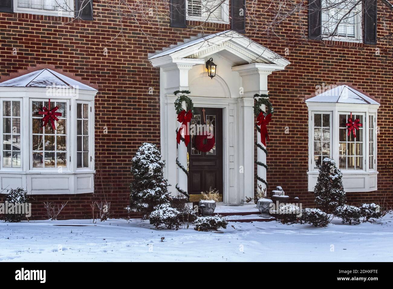 Entry and porch to traditional Georgian style brick house with columns and bay windows decorated for Christmas in the snow Stock Photo