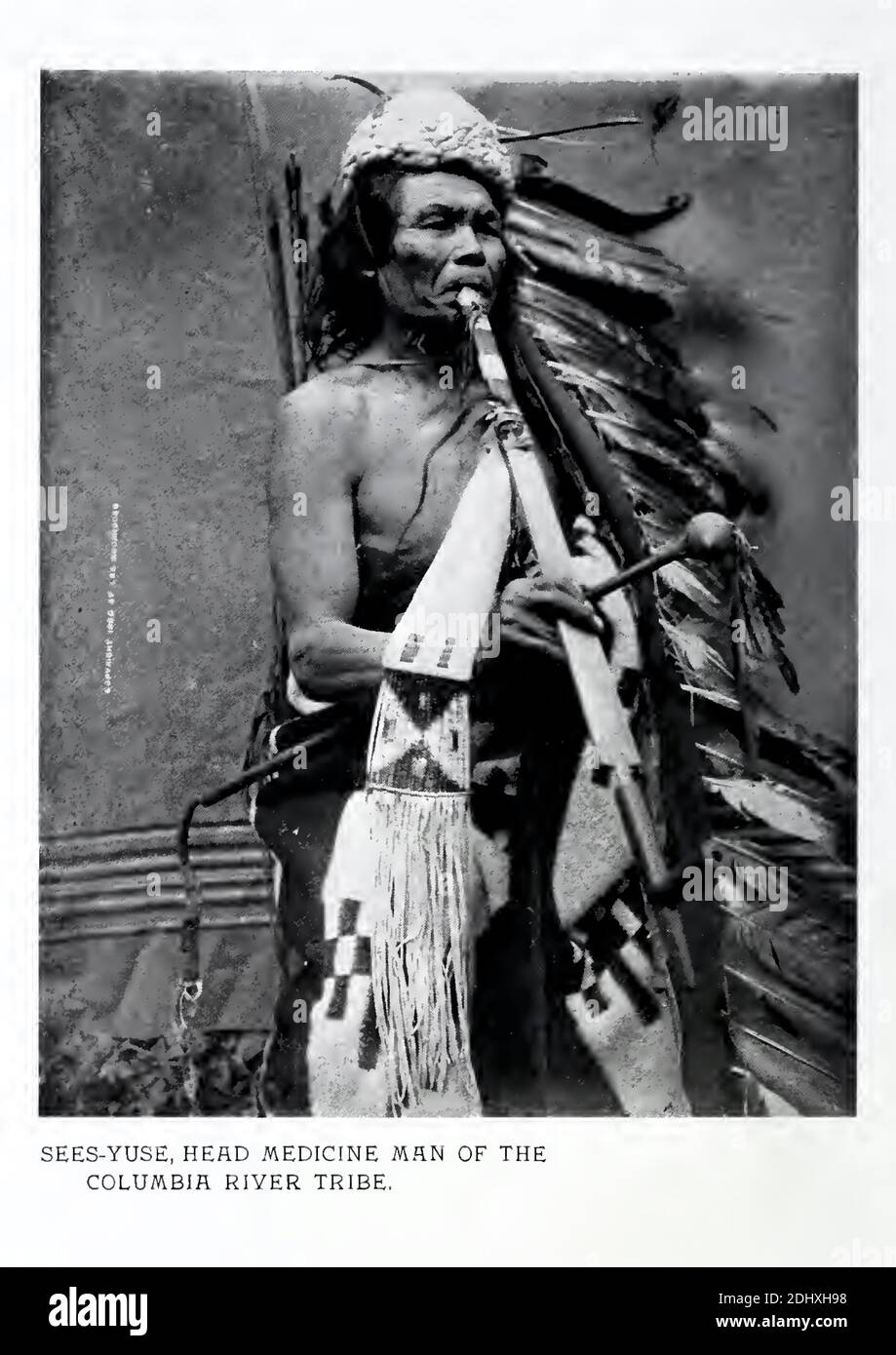 Lee Moorhouse photograph of Sees-Yuse the medicine man of the Columbia River tribe in tribal dress with peace pipe in hand and feathered  head-dress. Stock Photo