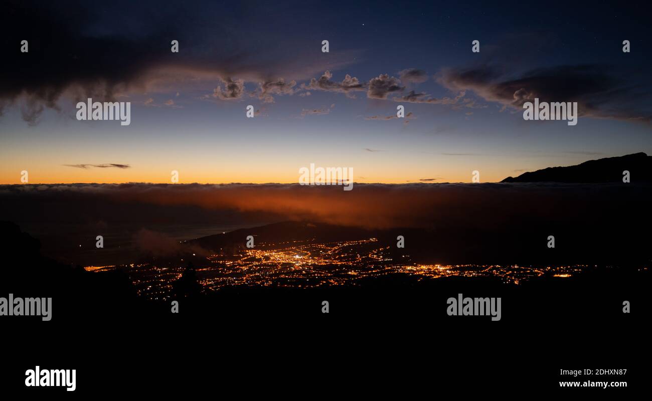 city lit at night seen from the mountain with clouds and stars in the sky Stock Photo