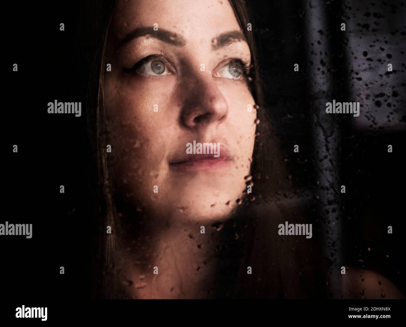 Beautiful woman behind wet window Stock Photo