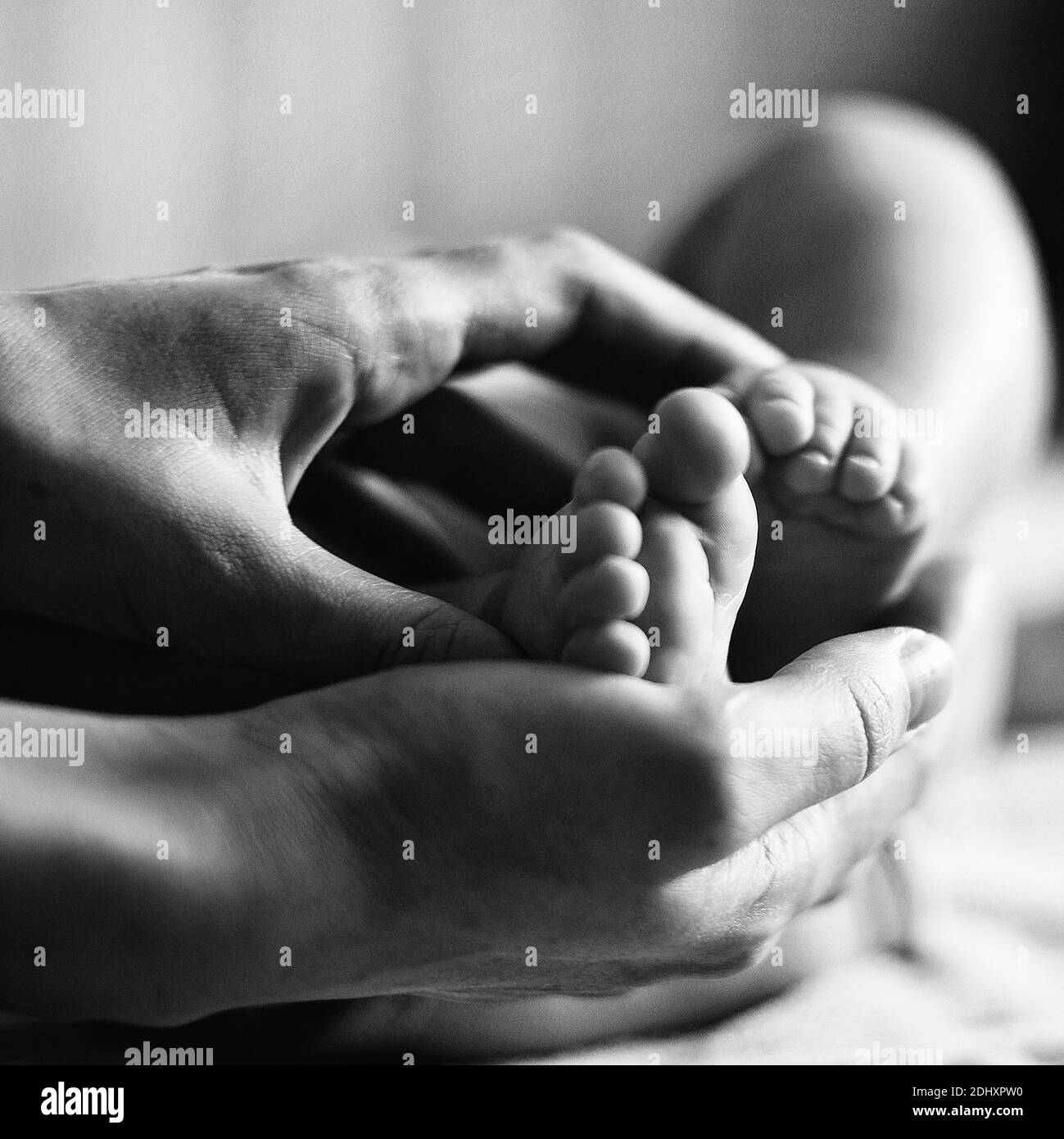 Father and mother hands holding small baby feet on bed at home. Top view. Close up. Beautiful conceptual image of parenthood. Stock Photo