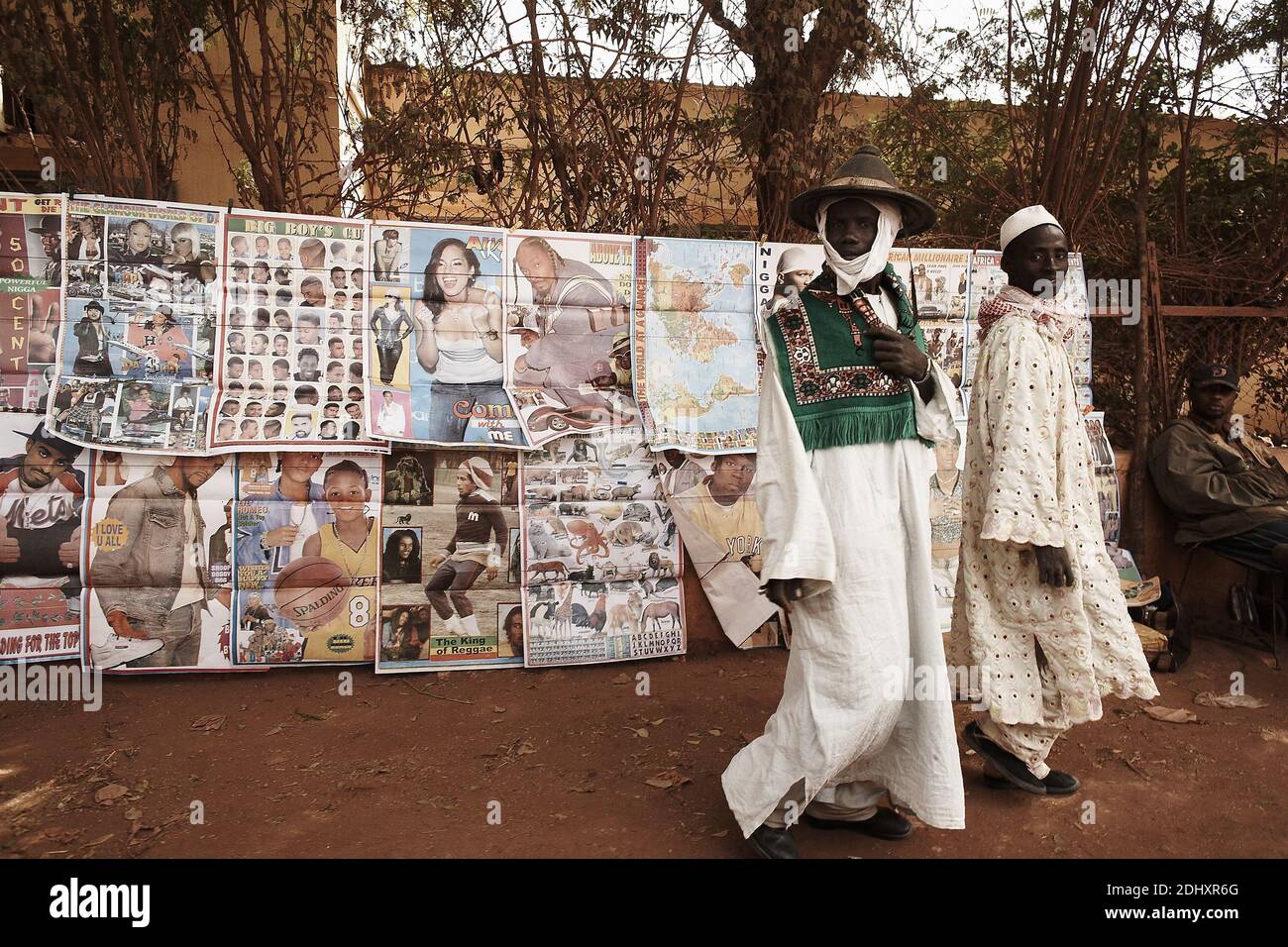 'In Mali, West Africa, two men dressed in traditional clothing engage with modern commerce by looking at popstar posters for sale Stock Photo