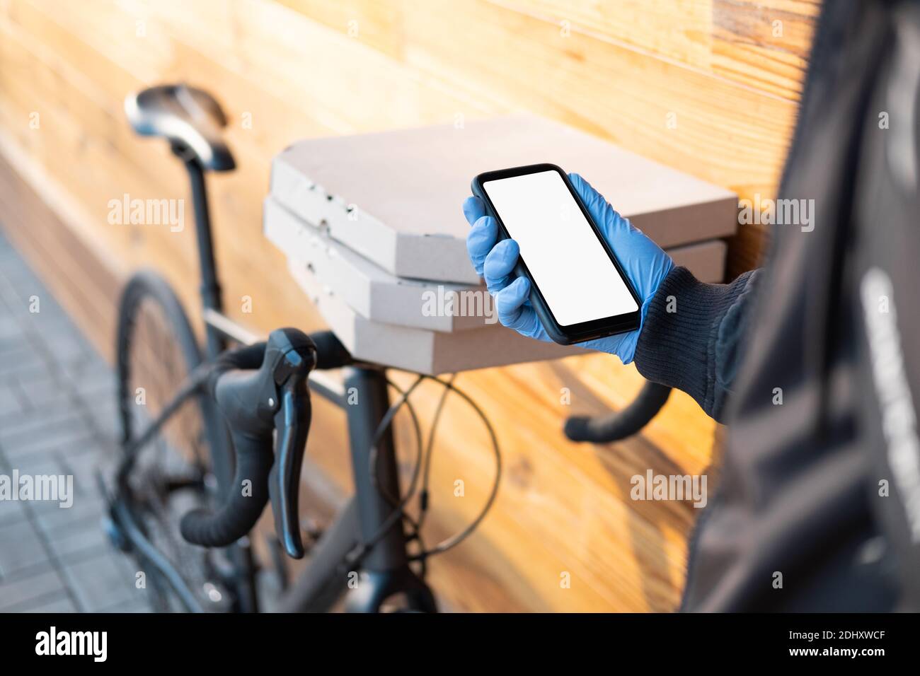 Delivery person standing next to a bicycle with pizza boxes holds a phone with whote screen. Job as a courier, bike messenger profession, part time wo Stock Photo