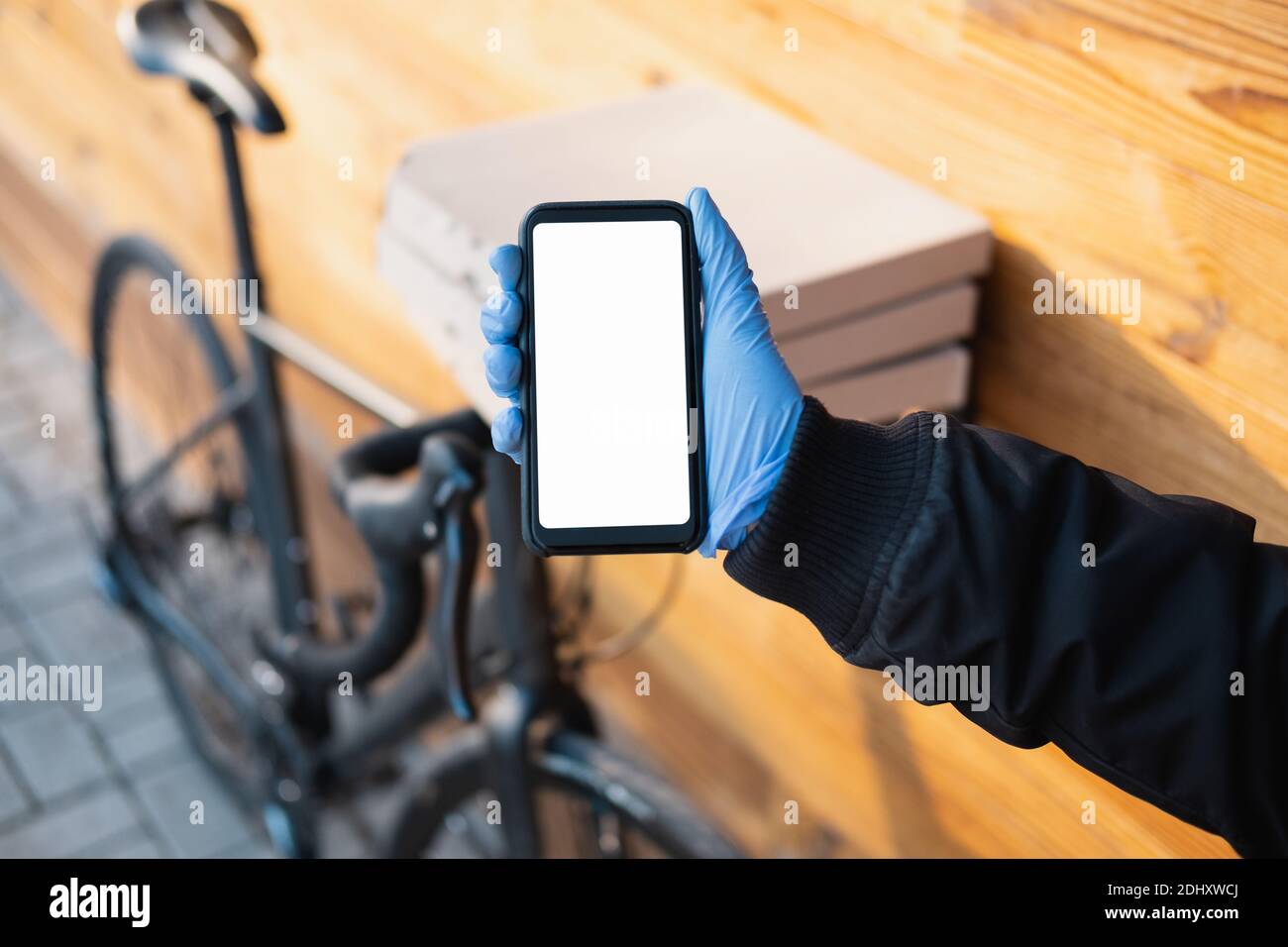 Delivery person standing next to a bicycle with pizza boxes holds a phone with whote screen. Job as a courier, bike messenger profession, part time wo Stock Photo