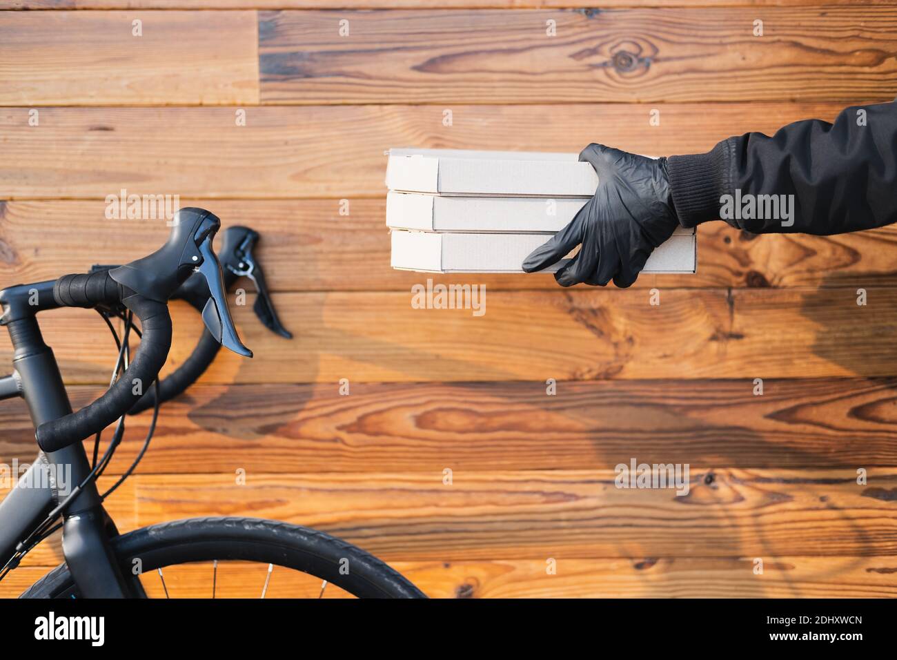 Pizza boxes in human hands next to a bicycle on wood background. Food
