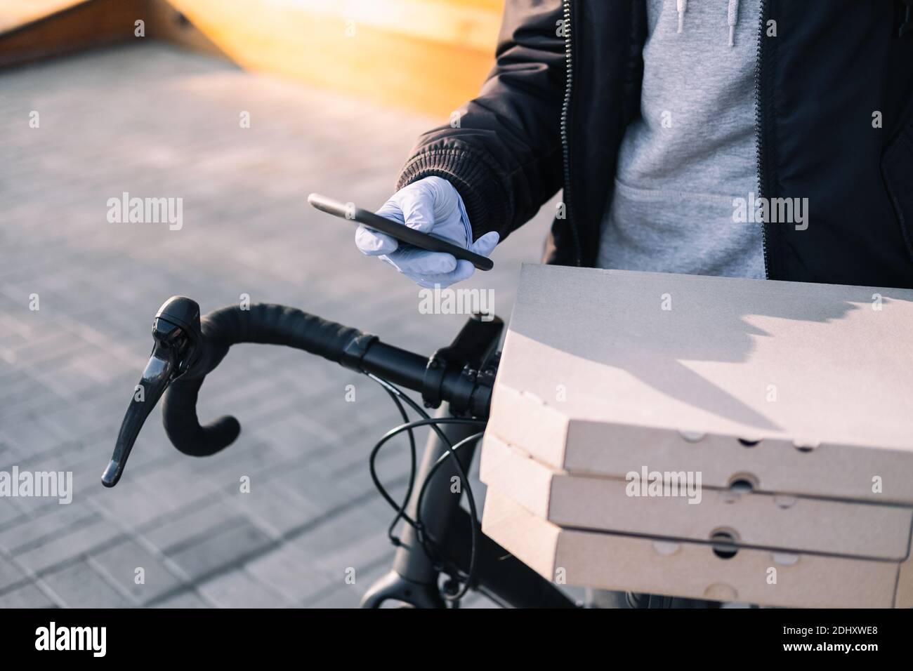 Delivery person standing next to a bicycle holds pizza boxes and a phone. Job as a courier, bike messenger profession, part time work concept Stock Photo