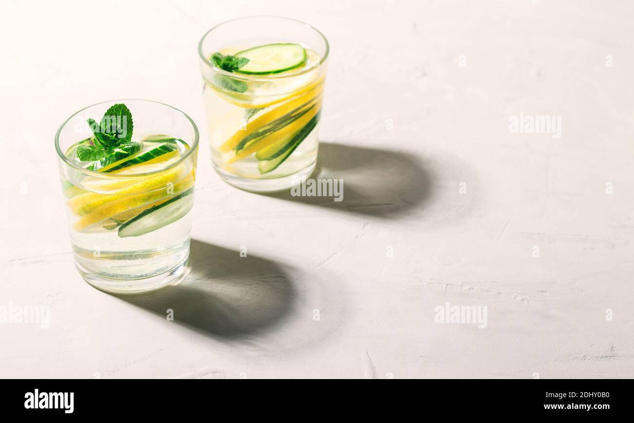 Sassy water for detox infused with lemon, cucumber and mint in glasses on white concrete background. Healthy lifestyle concept. Hard shadows. Space fo Stock Photo