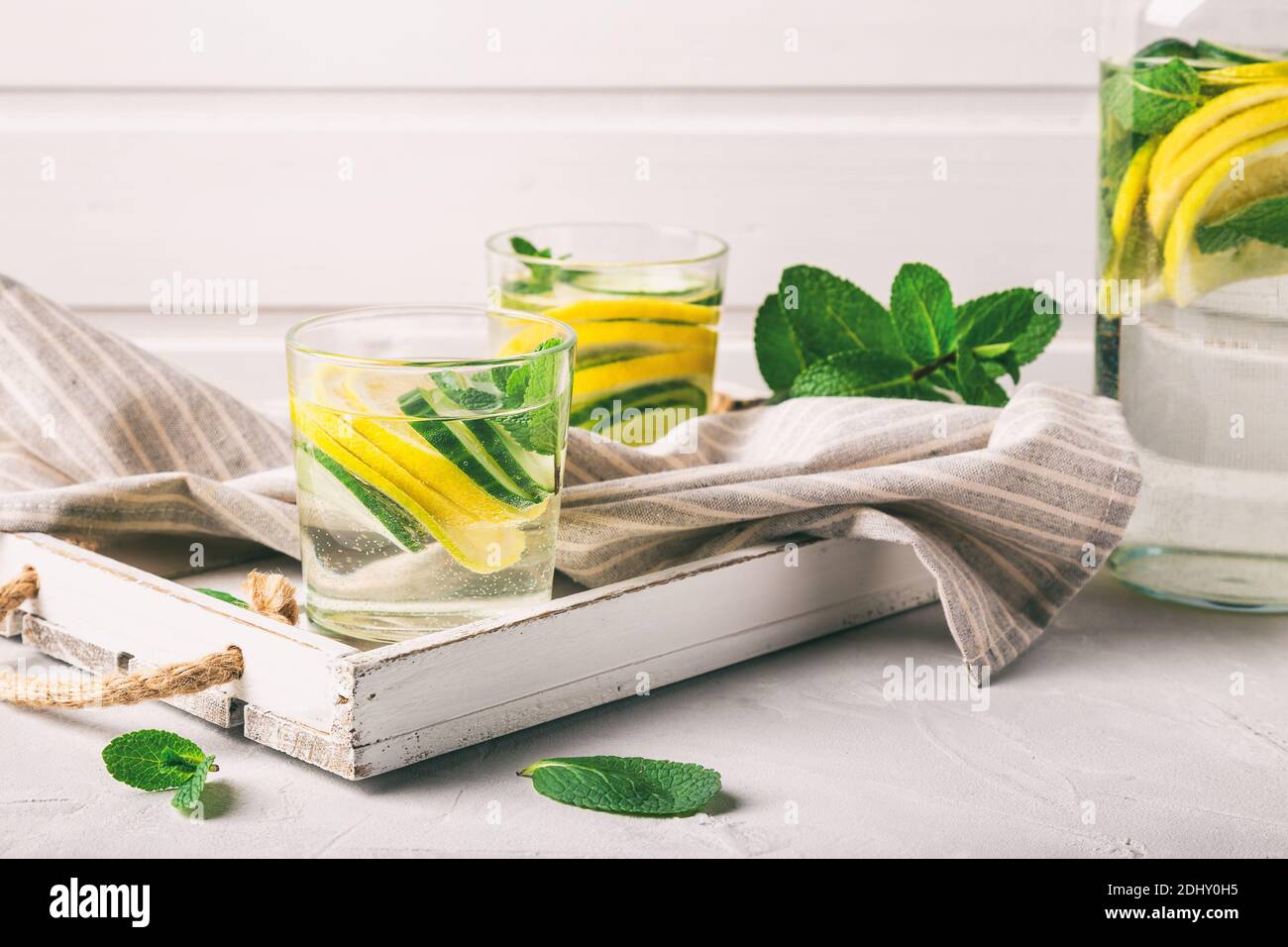 Sassy water for detox infused with lemon, cucumber and mint in glasses at white wooden tray. Healthy lifestyle concept. Stock Photo
