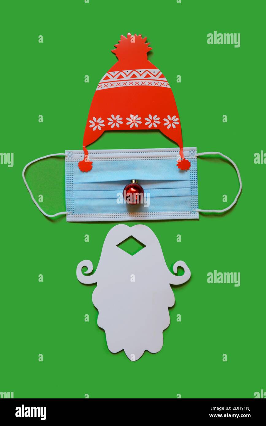 Santa Claus hat and beard with face mask on green background, creative minimal concept of Christmas and New Year Stock Photo
