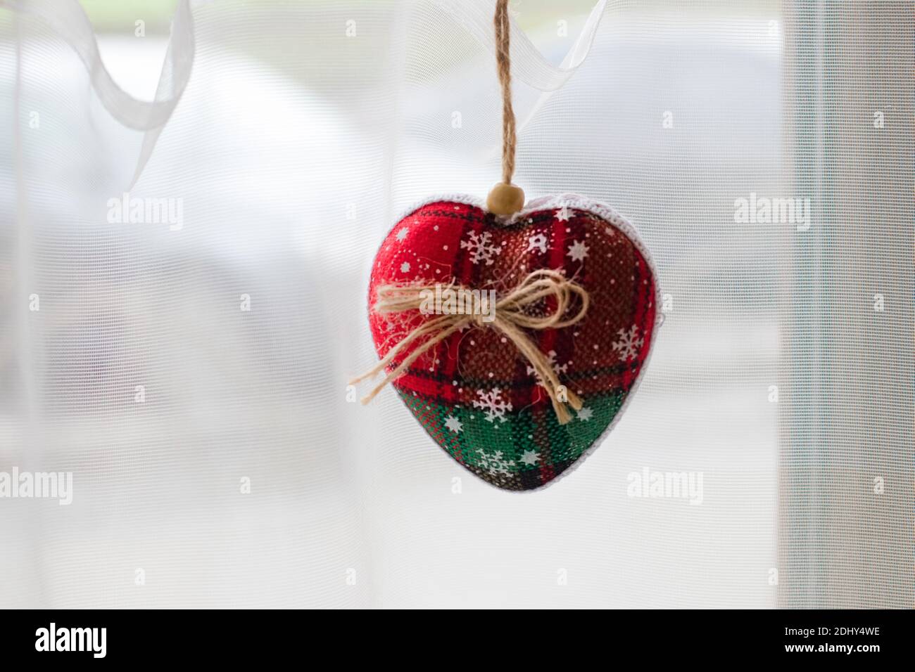 estive decor window. This handmade soft Christmas tree toy made of fabric of red and green color with a bow of string hangs on the window. New Year an Stock Photo