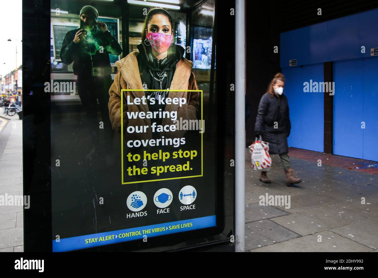 A woman wearing a face mask walks past a COIVD-19 public information campaign digital poster on display in London. Stock Photo