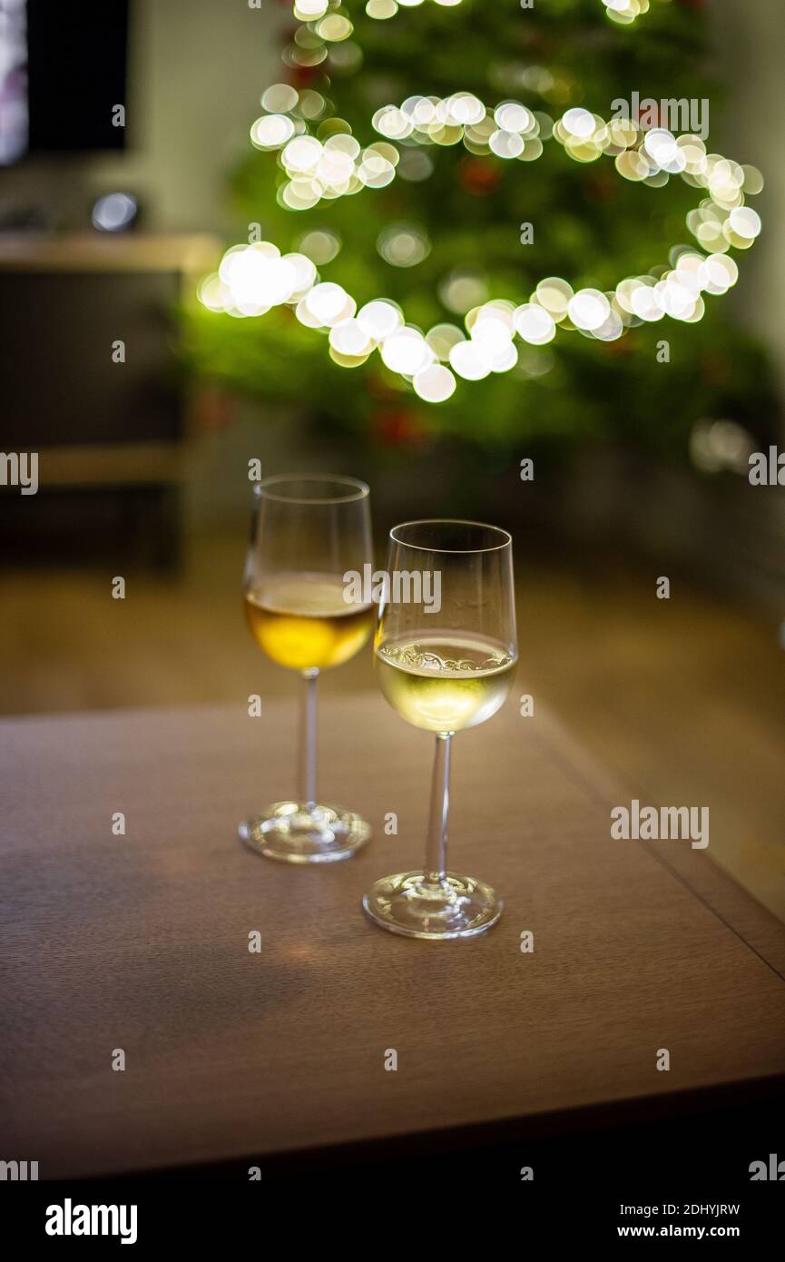 Two glasses of wine indoors at home in front of Christmas tree and lights on the wooden table Stock Photo