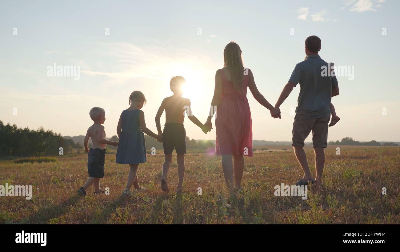 A friendly large family walks across the field at sunset with dog Stock ...