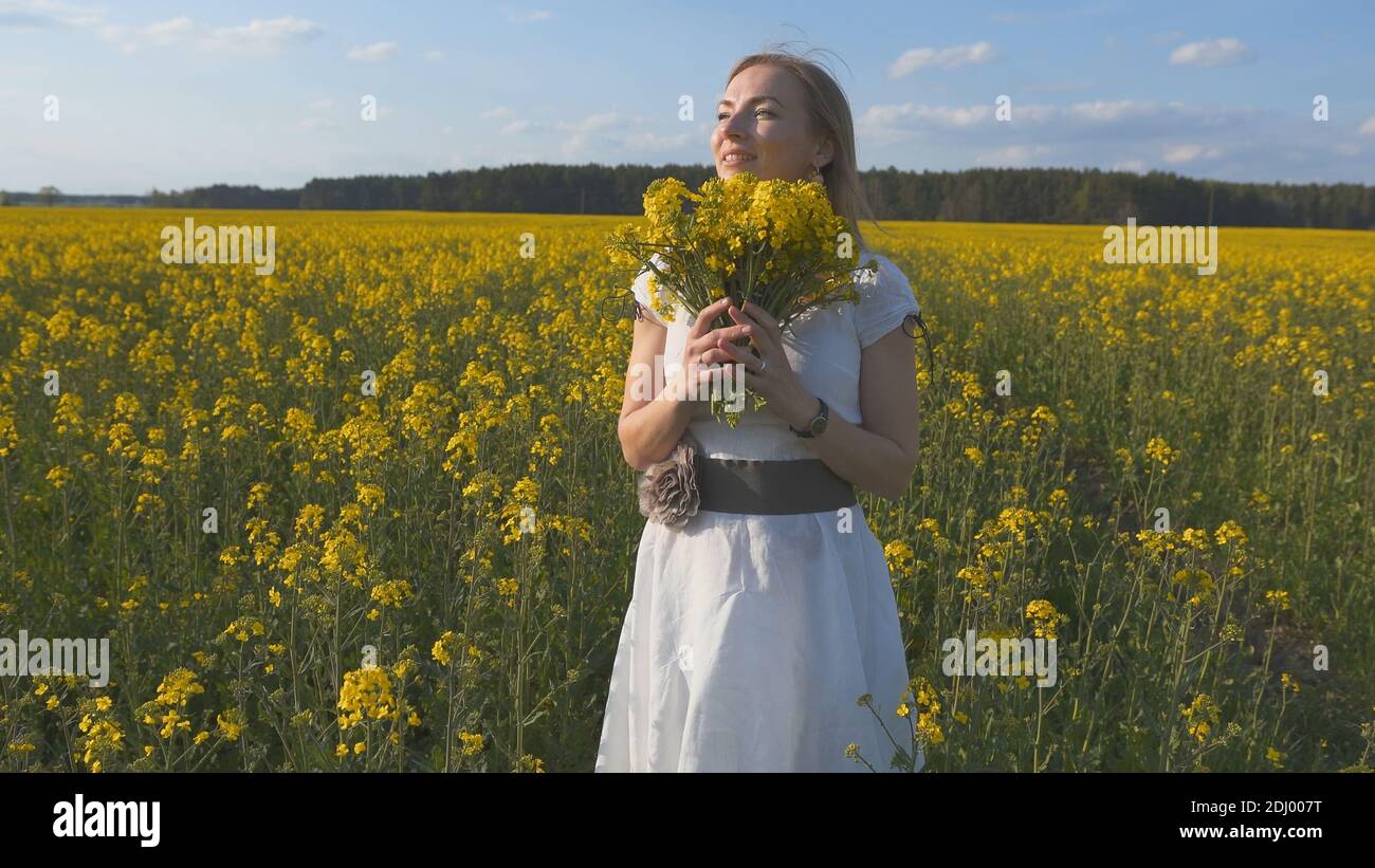 A girl in a white dress is walking among a rapeseed field Stock Photo ...