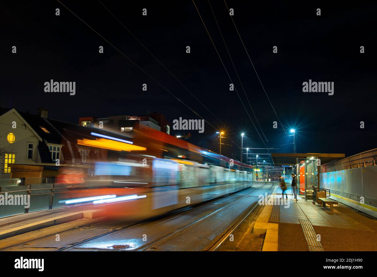 Tram passing a station in the night leaving a trail of light. Stock Photo