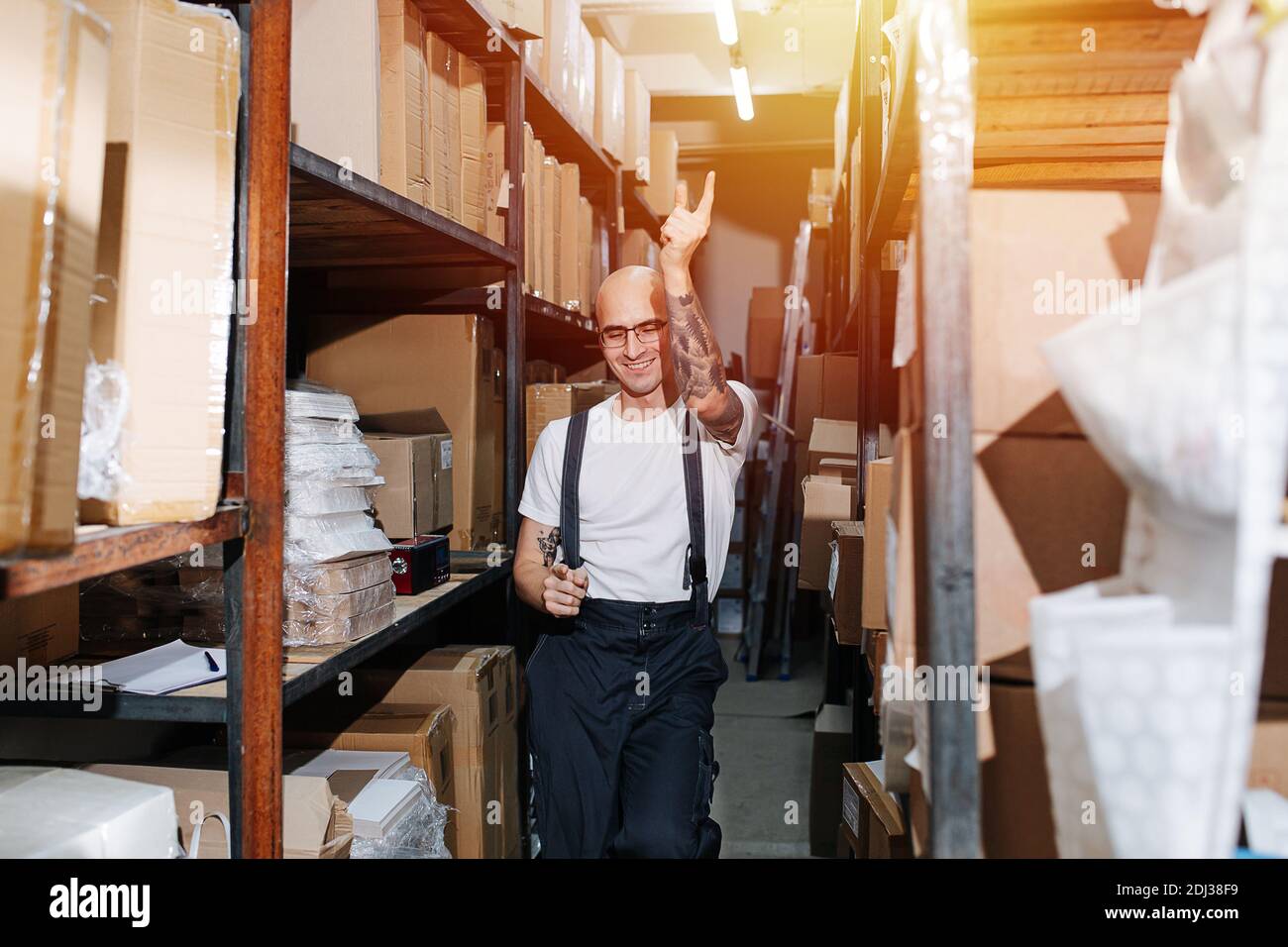 Smiling funny warehouse worker dance-walking between tall rows of shelves Stock Photo