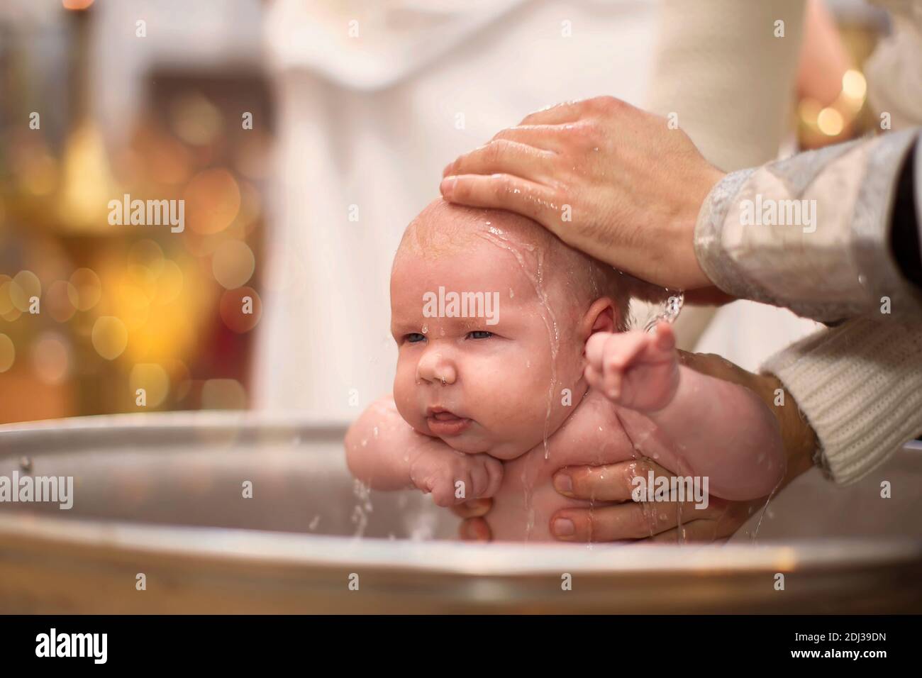 Orthodox baptism of a child.Baby in the baptismal font in the church. The hands of the priest pour water on the child during the ceremony of accepting Stock Photo