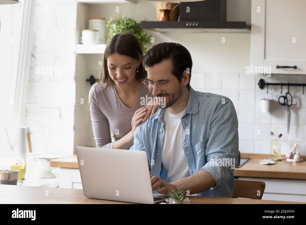 Happy young couple using laptop in modern kitchen together Stock Photo