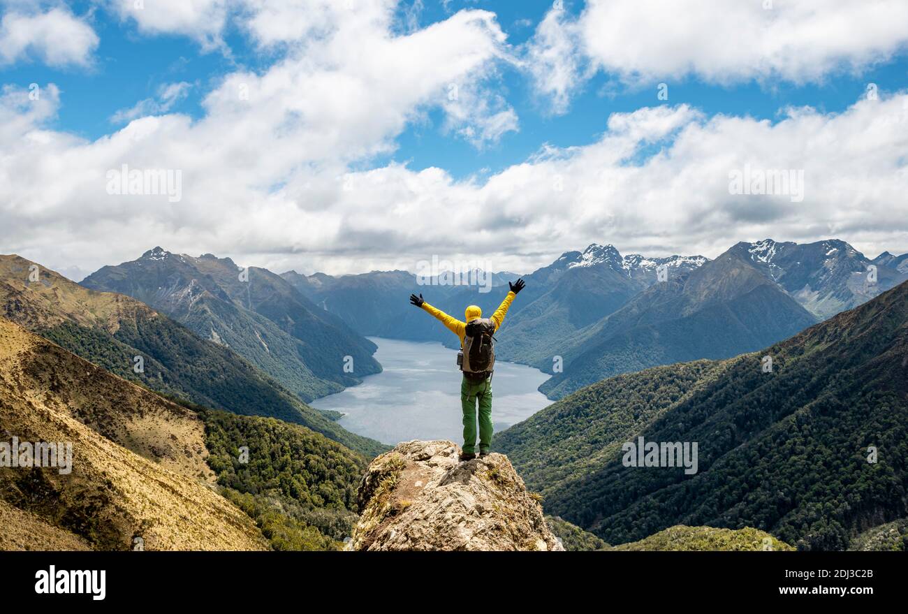 Mountaineer, hiker looks into the distance, stretching arms in the air, view of the South Fiord of Lake Te Anau, Murchison Mountains and Southern Stock Photo
