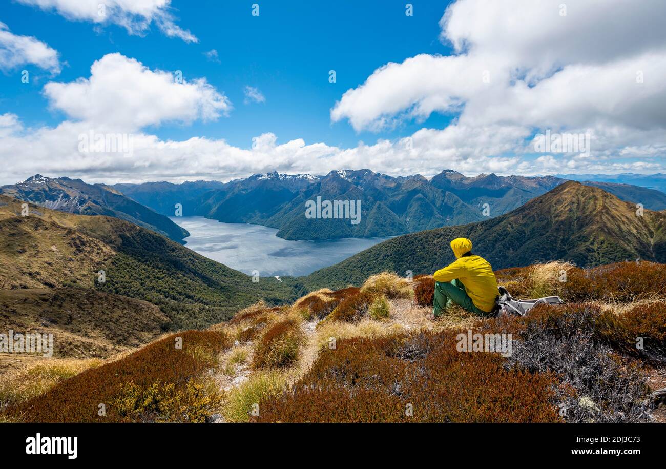 Mountaineer, hiker sitting in the grass, view of the South Fiord of Lake Te Anau, in the back Murchison Mountains and Southern Alps, on the hiking Stock Photo