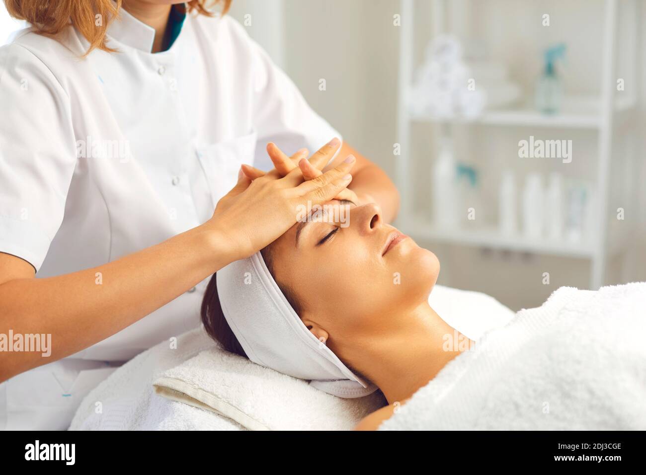 Hands of cosmetologist making facial massage for relaxed serene young woman Stock Photo