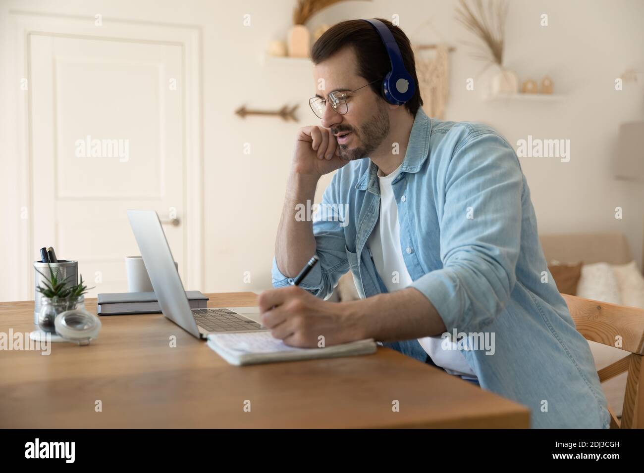 Serious man wearing glasses using laptop, writing notes, working online Stock Photo