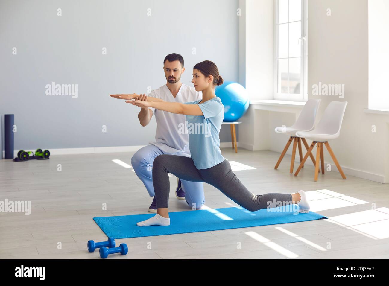 Man chiropractor fixing woman patients movements during exercising on fitness mat Stock Photo
