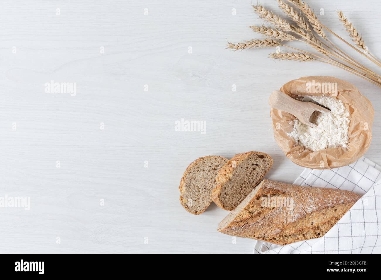 Loaf of bread with wheat ears and bag of flour on white wooden ...