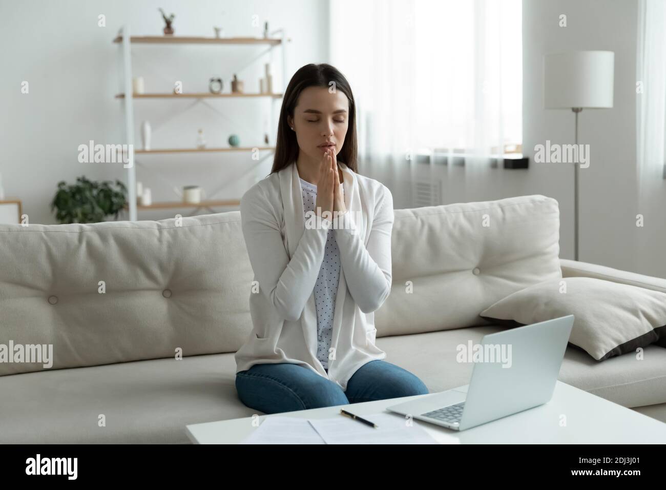 Calm young woman joining hands in prayer, asking help Stock Photo